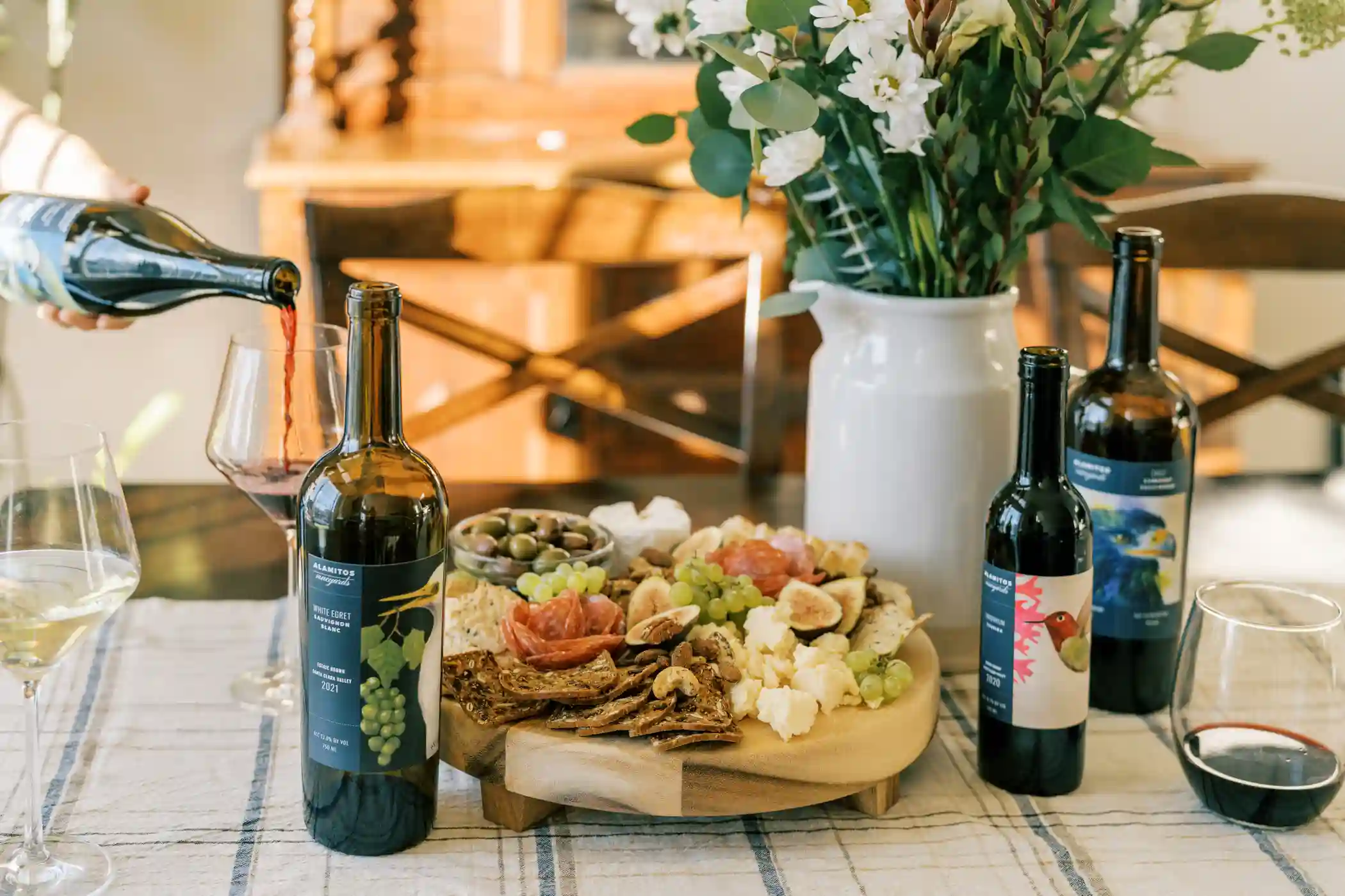 Charcuterie board, bottles of Alamitos wine, and a beautiful vase of flowers